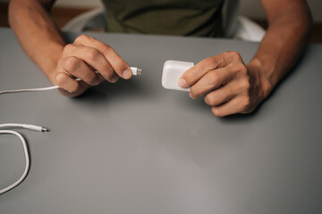 High-angle view of man connecting USB cable to electronic cigarette charger on gray desk,...