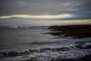 Rocky coastline with waves under cloudy evening sky