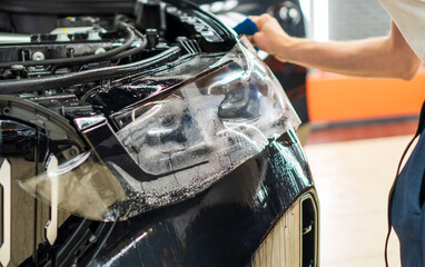 A car wrapping specialist applies a polyurethane film to the car. Selective focus. PPF protective film against chips and scratches. Car wrapping, detailing, tuning and styling. Detailer smoothes PPF. 