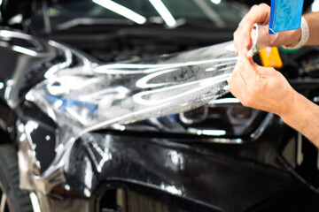 A car wrapping specialist applies a polyurethane film to the car. Selective focus. PPF protective film against chips and scratches. Car wrapping, detailing, tuning and styling. Detailer smoothes PPF. 