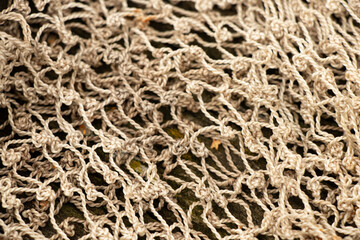 A close-up of an old fishing net made of light-colored rope lying on the ground, revealing the knot structure, interweaving