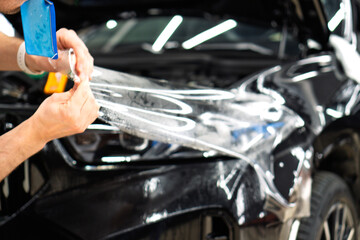 A car wrapping specialist applies a polyurethane film to the car. Selective focus. PPF protective film against chips and scratches. Car wrapping, detailing, tuning and styling. Detailer smoothes PPF. 