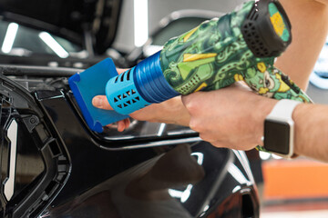 A car wrapping specialist applies a polyurethane film to the car. Selective focus. PPF protective film against chips and scratches. Car wrapping, detailing, tuning and styling. Detailer smoothes PPF. 