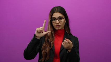Young hispanic woman in glasses making loser gesture on pink background, wearing red and black...