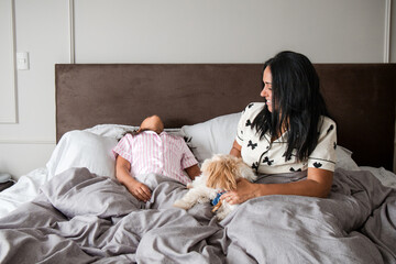 A woman is sitting on a bed with a child and a dog