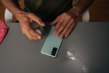 Close-up shot of unrecognizable man spraying disinfectant on smartphone, emphasizing hygiene and protection against germs and viruses sitting at table. Concept of healthy lifestyle.