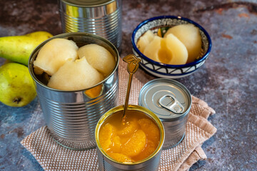 Canned pears and mandarin segments contrasted with two fresh pears, arranged on a rustic background. 