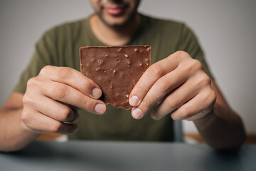 Cropped shot of man holding chocolate bar in front of chest, savoring its delicious aroma, preparing to indulge in delightful sweet treat that promises pure enjoyment, at table on isolated background