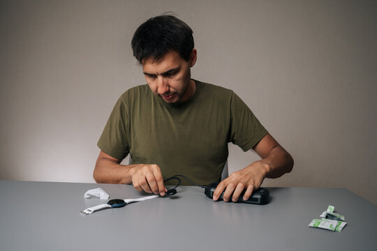 Front view of man connecting smartwatch to portable charger, preparing for outdoor activities, ensuring continuous functionality, sitting at table on isolated background. Concept of healthy lifestyle