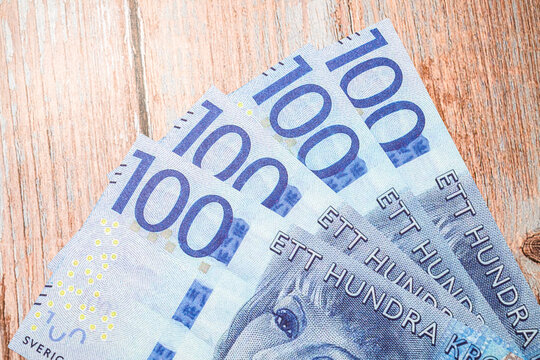 Close up of Swedish hundred kronor bills fanned out on wooden background.