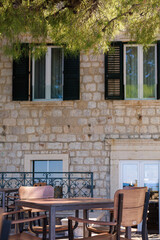 Rustic stone house with wooden table and chairs in a shaded courtyard under greenery. Concept of old town lifestyle, outdoor decor and Mediterranean charm.