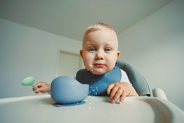 Cheerful baby enjoys mealtime adventure with cereal and playful utensils in a bright and clean kitchen setting