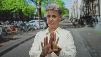Fototapeta premium Woman holds up both hands in a repel gesture on a sunny urban street beside parked bicycles on the sidewalk; disgust.