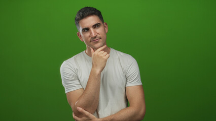 Man with hand on chin in green studio, hand touching chin while looking to the side; pensive...