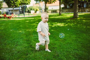 Enjoying a sunny day in the park, a young child runs toward floating bubbles with wonder and excitement while surrounded by greenery and play equipment