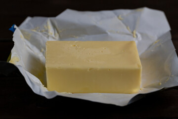 Piece of butter on wrapping paper on dark wooden table