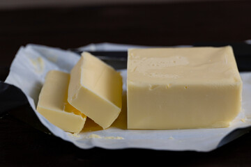 Fresh butter block with slices and knife on paper