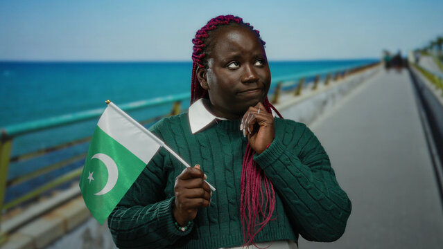 Woman holding pakistan flag standing on seaside promenade with ocean backdrop expressing diversity and cross-cultural connection through travel and tourism outdoors.