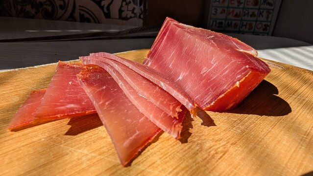 Elegant cured ham on rustic wooden surface with dramatic lighting