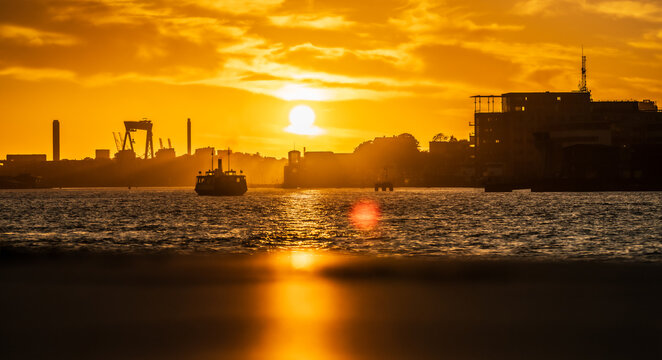 Silhouette ferry crossing city harbor under dramatic orange sunset.