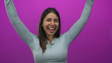 Hispanic woman celebrating with raised arms and a joyful expression against an isolated pink background wall showcasing happiness and success.