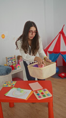 Woman organizing toys in a colorful kindergarten classroom with educational materials around,...