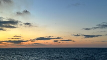 Soft pastel ocean sunset with glowing horizon and scattered clouds