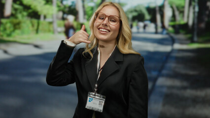 Woman gesturing call me in a park with trees wearing a business suit and id badge, smiling...