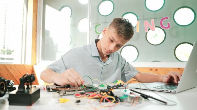 Smart happy boy inspect or learning to use electronic tool to fix car model. high school student studying about electric equipment to repair robotic machines while sitting at STEM class. Edification