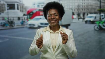 Woman smiling confidently outdoors on a bustling city street wearing a white blazer with iconic red double-decker buses passing by in the background.