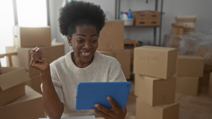 Woman talking on a video call in a new home surrounded by moving boxes, using a tablet in the living room, wearing a sweater and enjoying her new apartment.