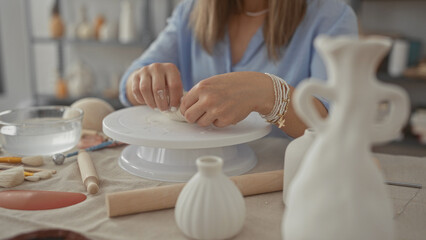 Woman shaping clay vessel with hands on white pottery wheel in studio surrounded by ceramic tools and vases; serenity creativity mastery innovation.