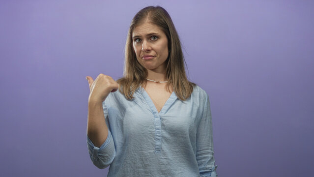 Woman pointing thumb to side with raised eyebrow and pursed lips wearing loose linen blouse in purple studio; doubt.