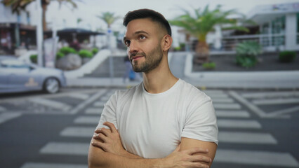 Young man standing confidently on urban street with trees in background displaying a relaxed demeanor in vibrant city setting under clear skies.