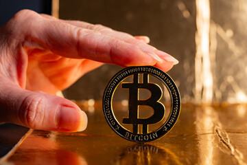 Close Up of Hand Holding Physical Gold Bitcoin Coin on Reflective Golden Surface