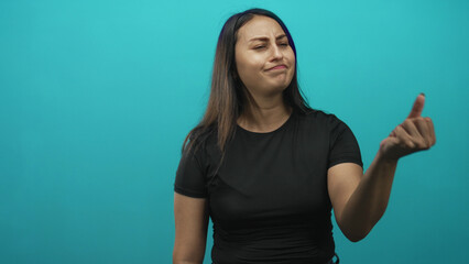 Young hispanic woman finger to lips then reluctant thumbs up in studio with turquoise wall while...