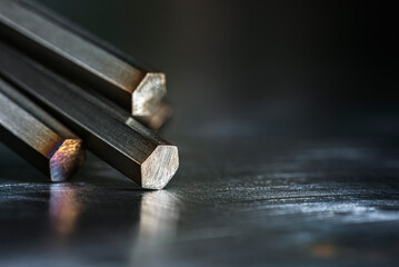 Non-ferrous metal rods lying on a metal surface in a dark, industrial space