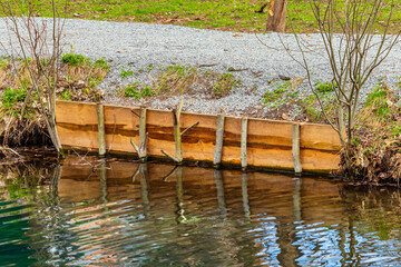 Strengthening the shore with wooden planks and timber. Erosion control and soil protection from collapse. Close-up of a pedestrian walkway along the water's edge