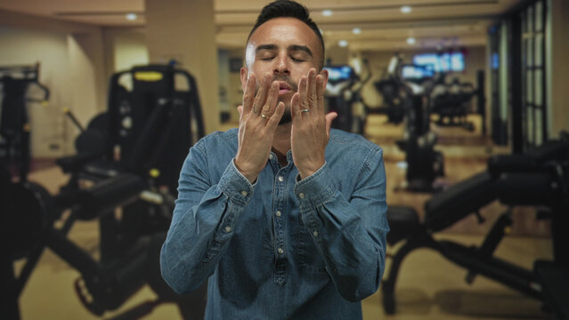 Man blowing a kiss with both hands toward camera in a gym studio filled with blurred exercise machines and cardio equipment; affection. - Powered by Adobe