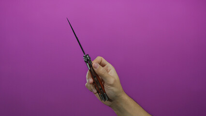 Man's hand holding a switchblade knife against a vibrant pink background, showcasing the knife's...