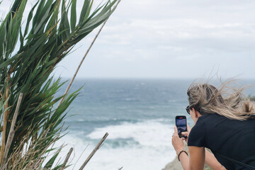 Frau fotografiert Atlantikk&uuml;ste im Baskenland mit Smartphone, windiger Tag