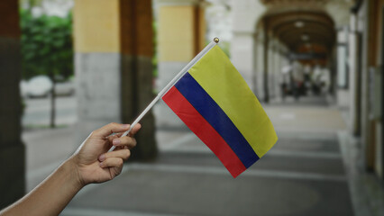 Hand of caucasian male holding colombian flag outdoors on a city street, symbolizing national pride...