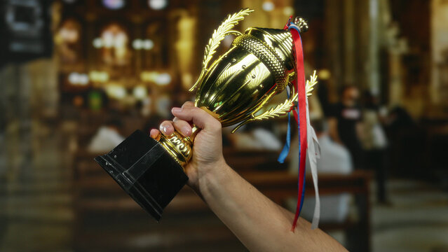Man holding a golden trophy with ribbons inside a church, highlighting achievement and the significance of indoor celebrations.