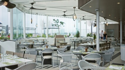 Obraz premium Soft blurred cafe interior showing a bright terrace dining area with woven chairs, tiled floor, tables, ceiling fans and glass walls; background copyspace overlay calm.