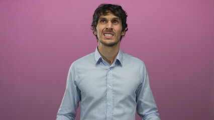 Man covers ears with hands against bright pink studio wall while grimacing in discomfort; frustration.