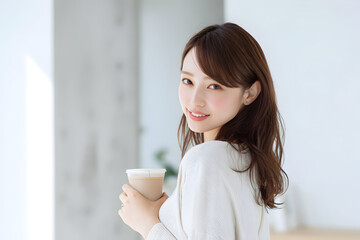 カフェタイム テイクアウトカップを手に微笑む若い女性の室内ポートレート 明るい自然光が差し込むライフスタイルイメージ
