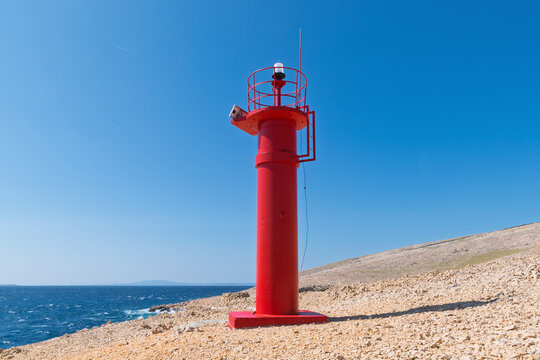 Red lighthouse on rocky coastline under clear blue sky. Baška, Krk Island, Croatia