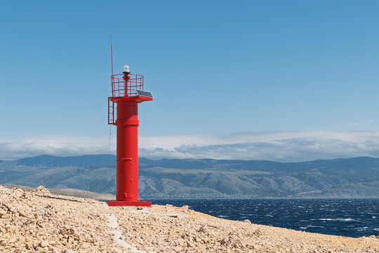 Red lighthouse by the sea with mountains and clear blue sky. Baška, Krk Island, Croatia