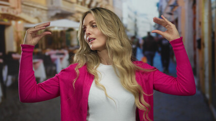 Woman lifts hands gesturing outdoors as a young blonde stands on a terrace outside a restaurant by...
