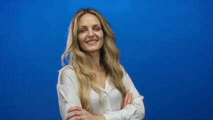 Woman posing confidently with arms crossed against a vibrant blue background, wearing a white shirt and displaying a calm expression, highlighting modern simplicity and elegance.